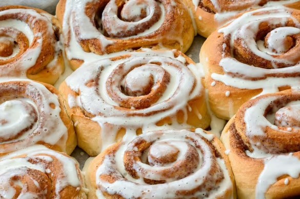 A delicious plate of cinnamon rolls, freshly baked and topped with a generous drizzle of creamy icing. The rolls are golden brown and soft, with a perfect swirl of cinnamon filling visible in each bite.